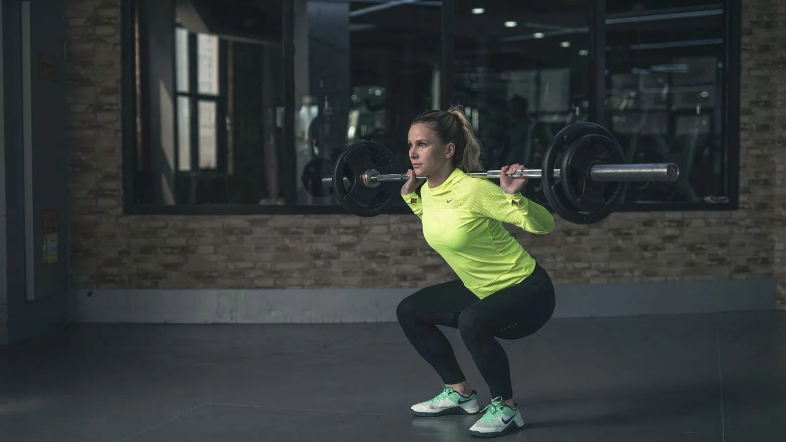 A woman performing a barbell squat in an empty gym
