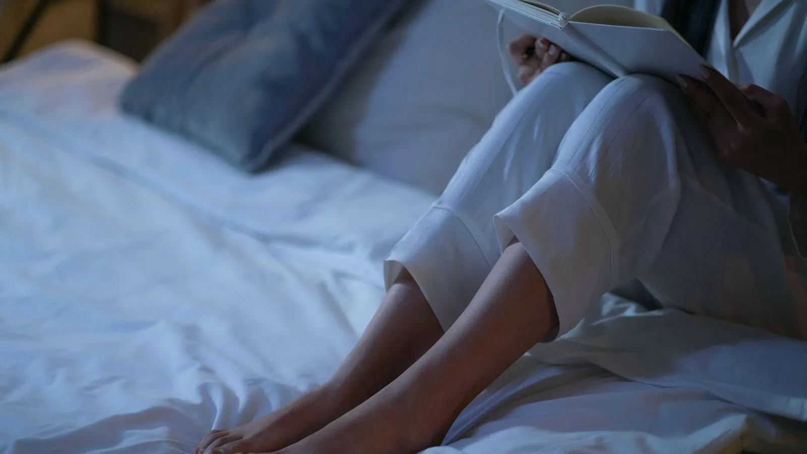 The legs of a person sitting on a bed with blue-lit sheets at night