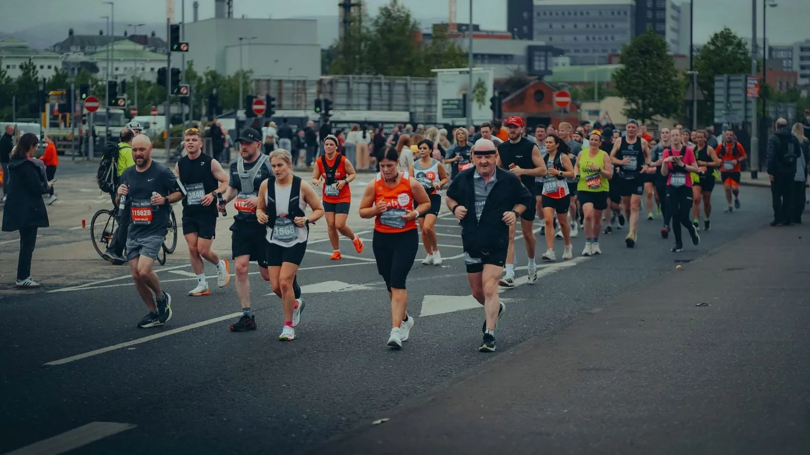 Runners in a city marathon moving along a wide road, with spectators at the roadside