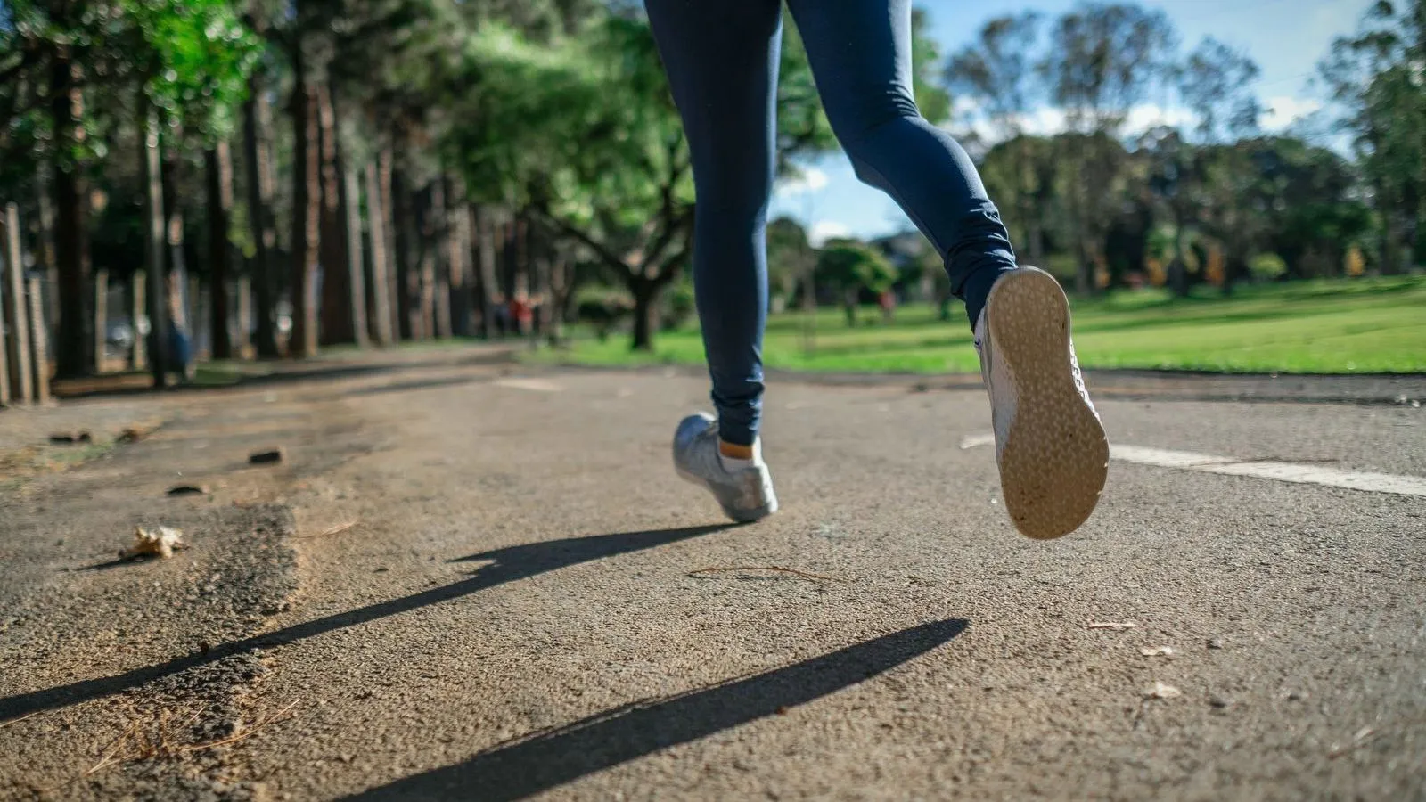 The legs of a runner on a park path, seen from behind, with the sole of one shoe lifted.