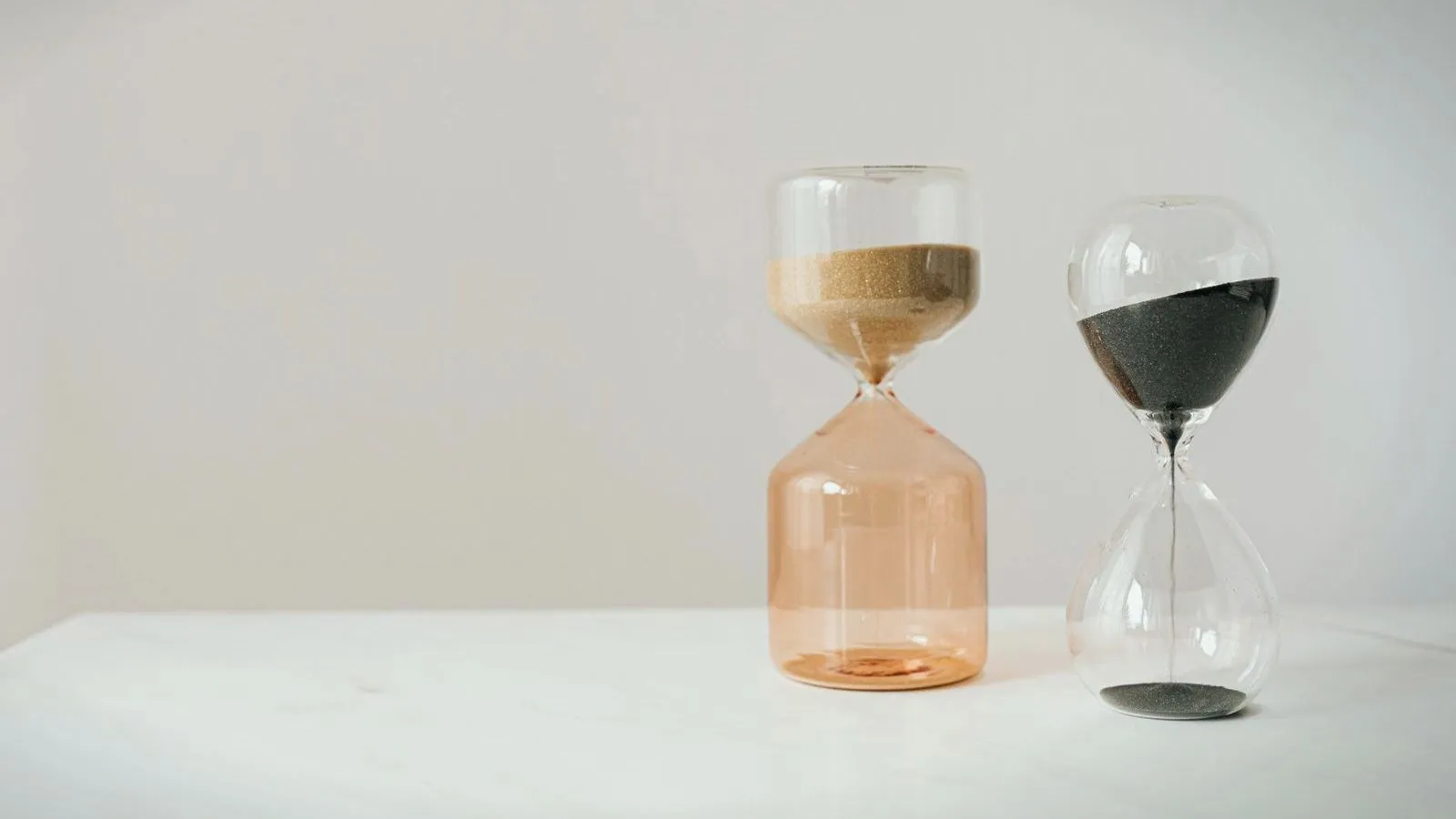 Two hourglasses side by side on a white surface, one with pale sand and one with dark