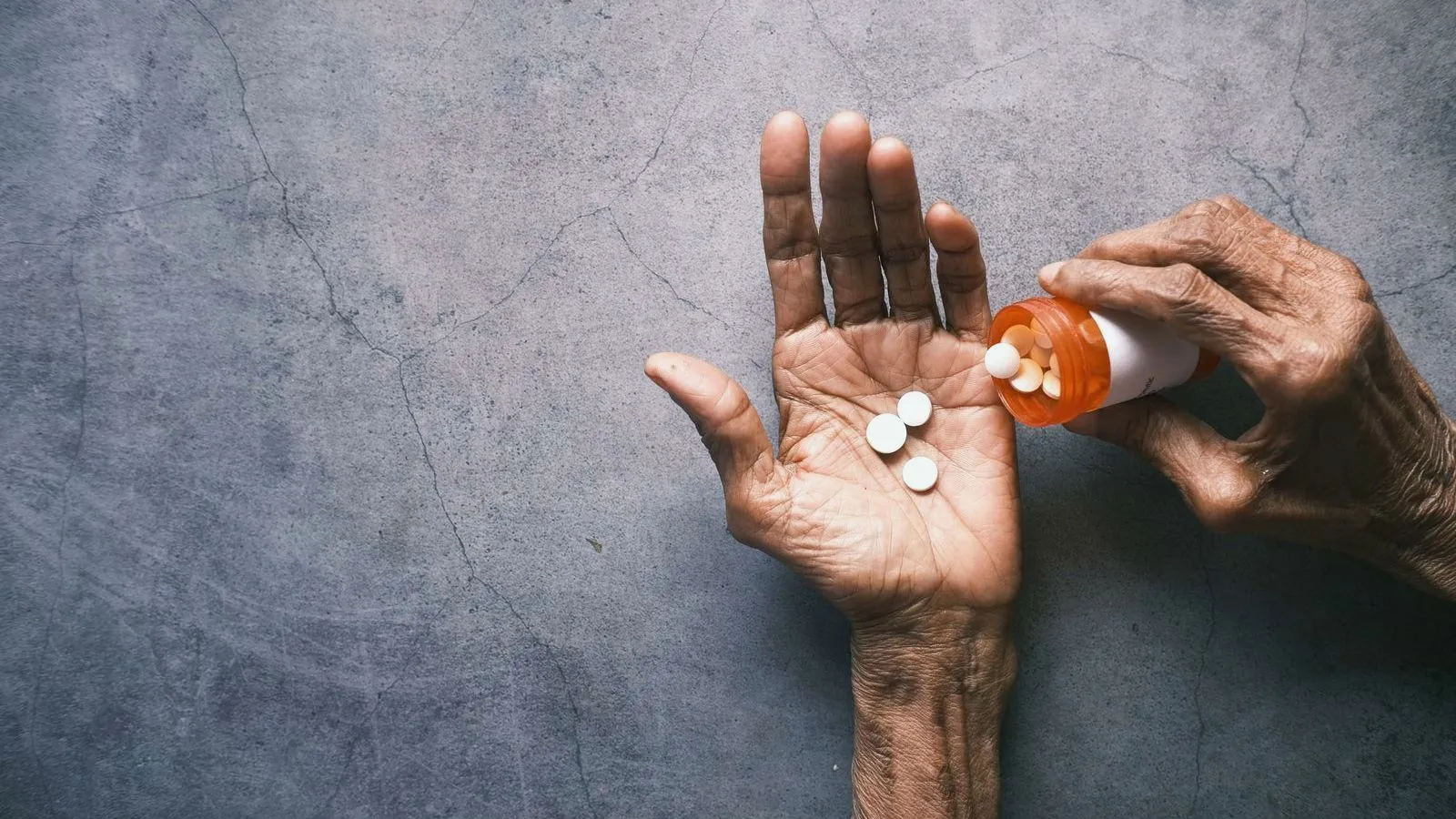 An aged hand tipping white tablets from an amber bottle into an open palm