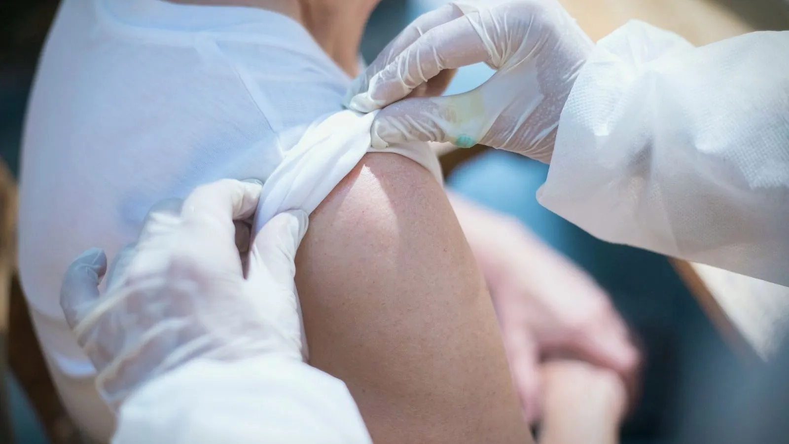 Gloved hands pressing a dressing onto a bare upper arm after an injection