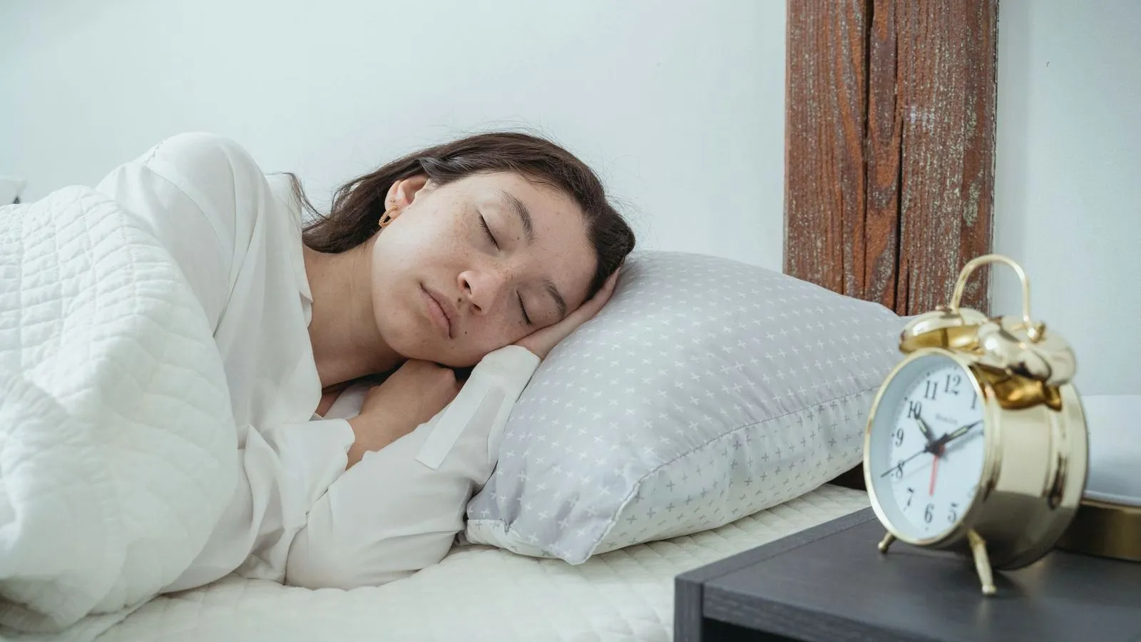 A woman asleep on her side with a gold alarm clock on the bedside table