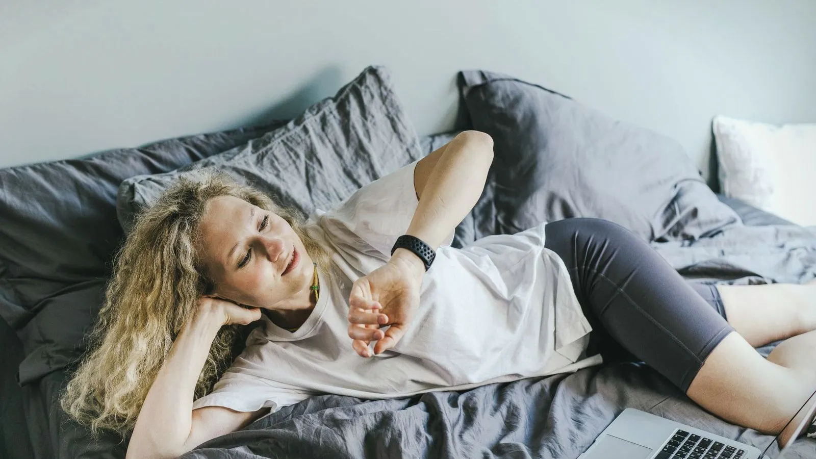 A woman lying on a bed looking at a fitness tracker on her wrist