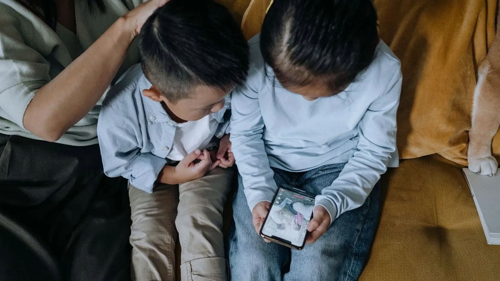 Two children on a couch, seen from above, looking at a phone that one of them is holding.