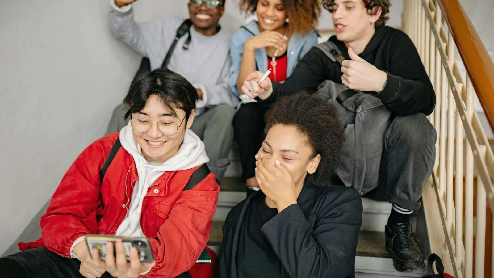 A group of teenagers sitting on a staircase looking at a phone