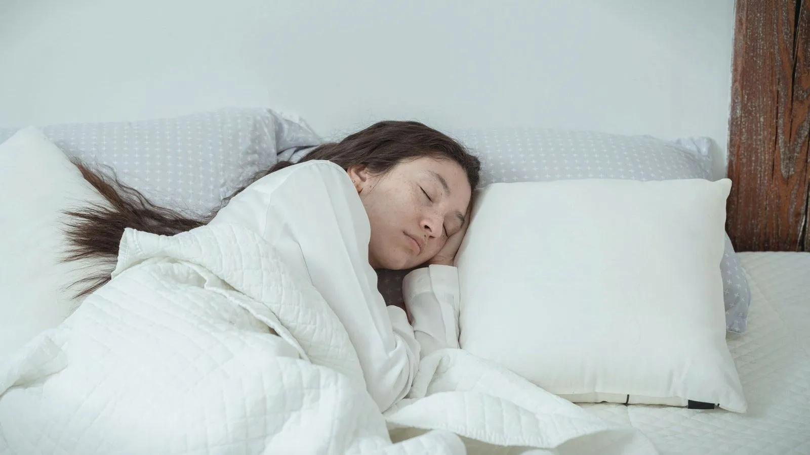 A young woman asleep under a white blanket with her head on a white pillow.