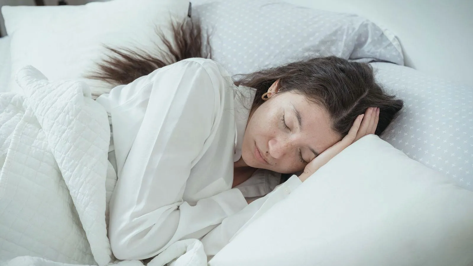 A woman asleep on her side on white pillows with a hand beneath her head