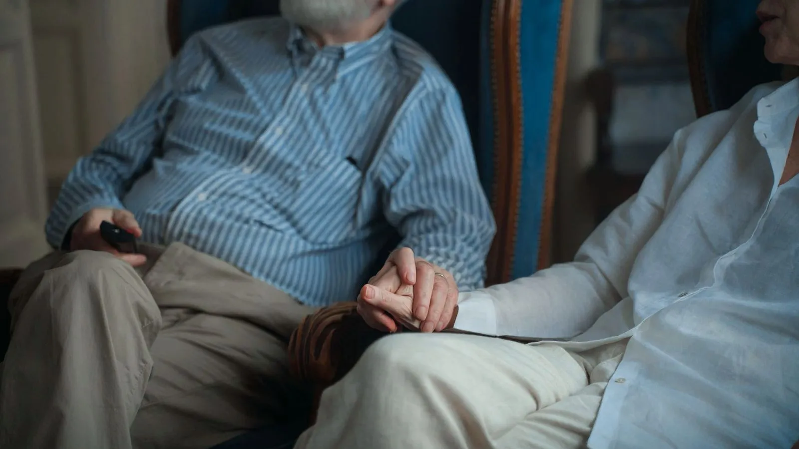 An older couple sitting side by side in armchairs, holding hands