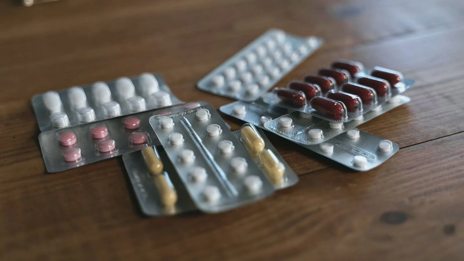 Several part-used blister packs of different tablets and capsules on a wooden table