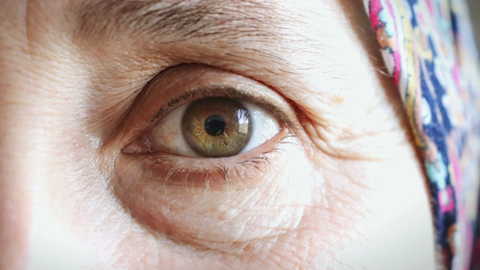An extreme close-up of an older person's eye, hazel iris surrounded by lined skin