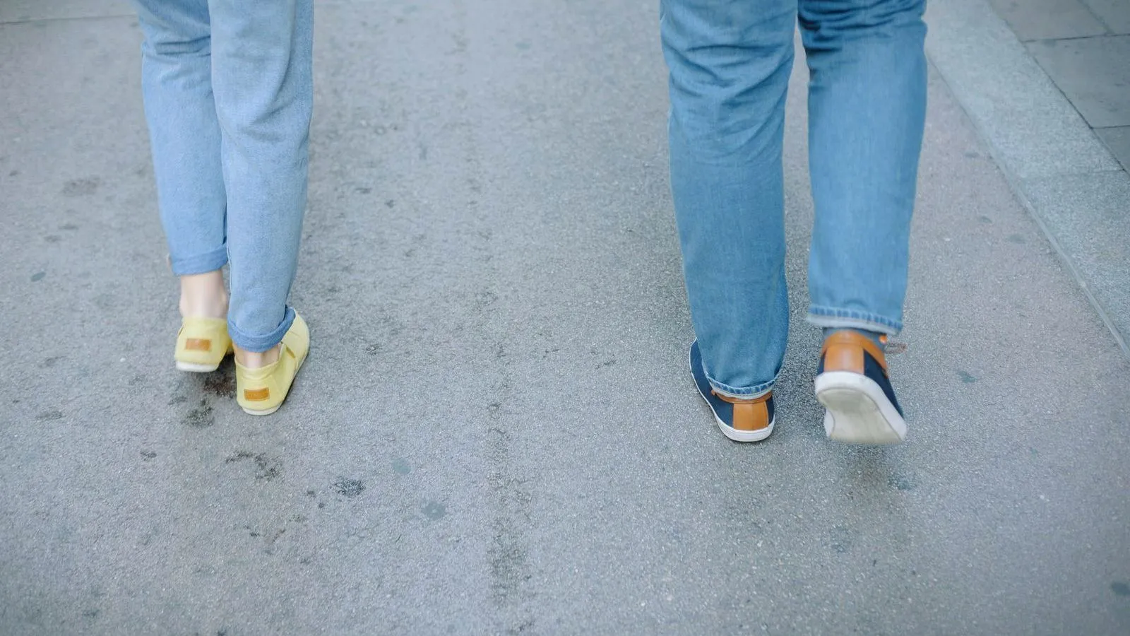 Two people in jeans walking along a pavement, seen from behind at ankle height