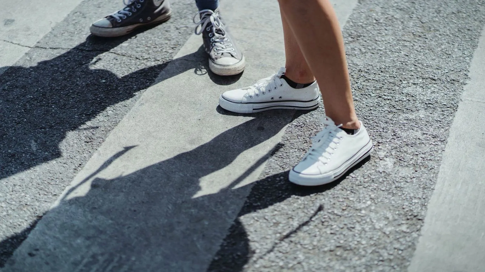 Two people in canvas sneakers walking across a sunlit street.