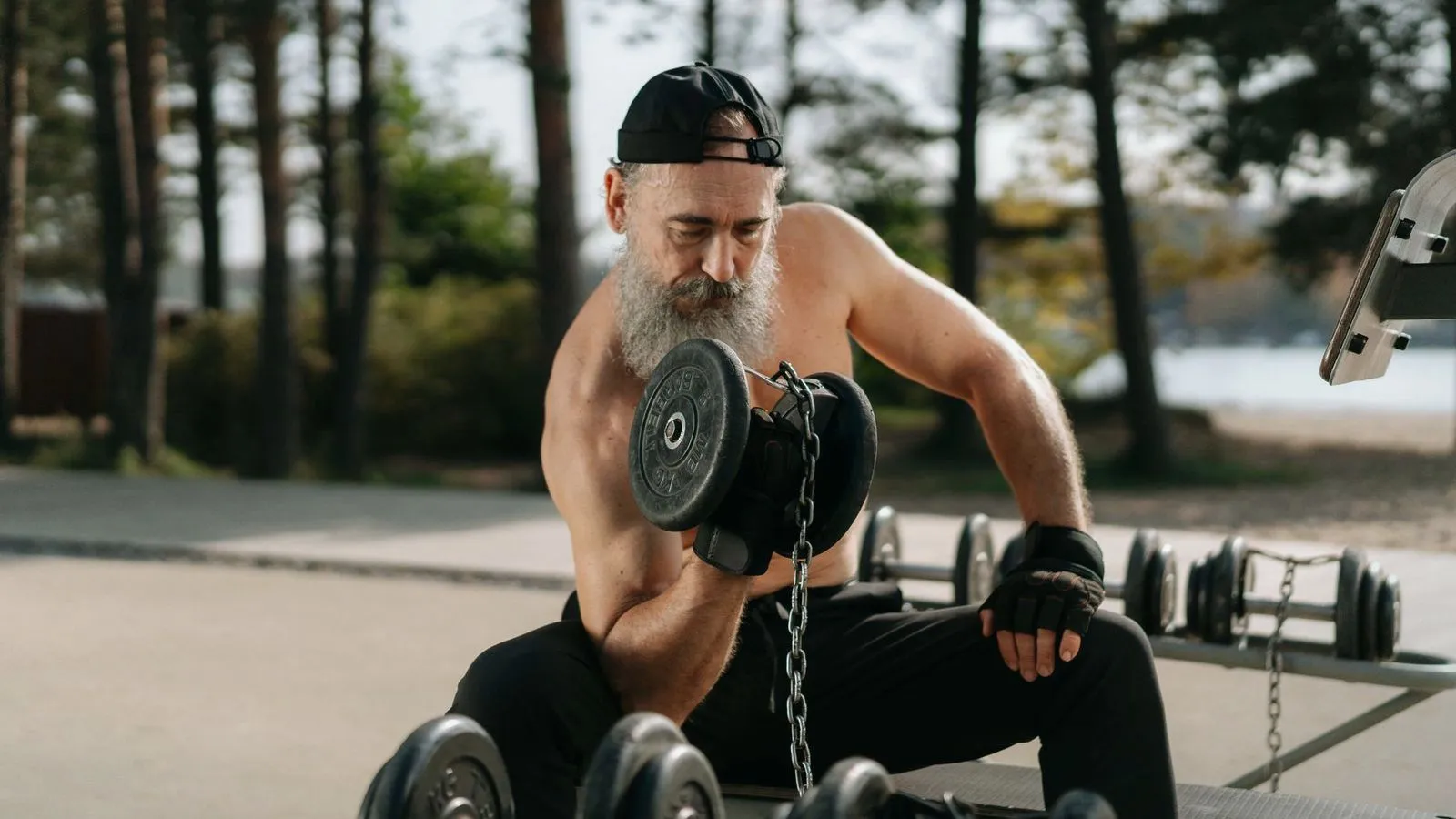 A bearded older man doing a dumbbell curl at an outdoor gym
