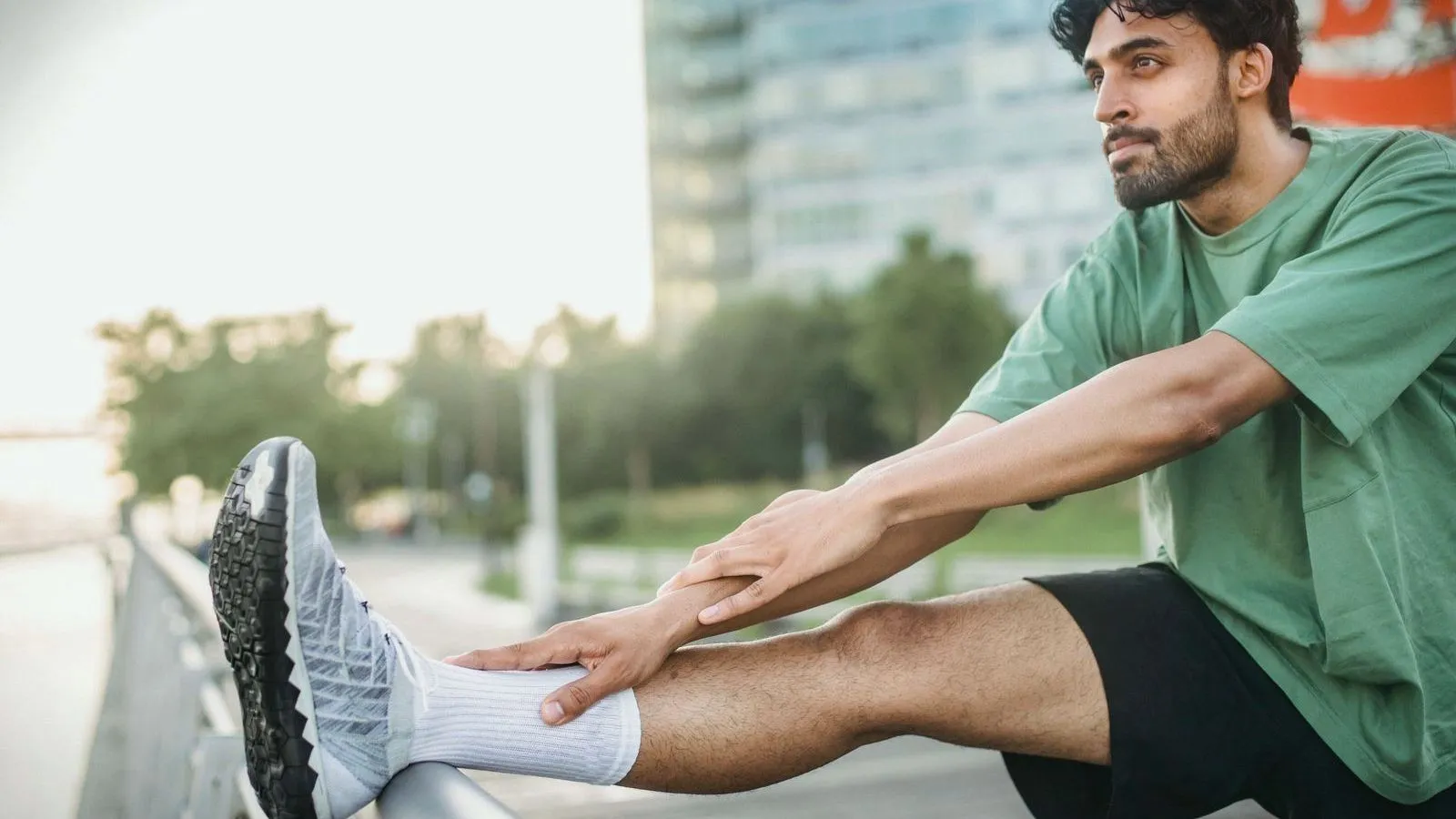A man stretching his leg on a railing outdoors, holding his ankle.