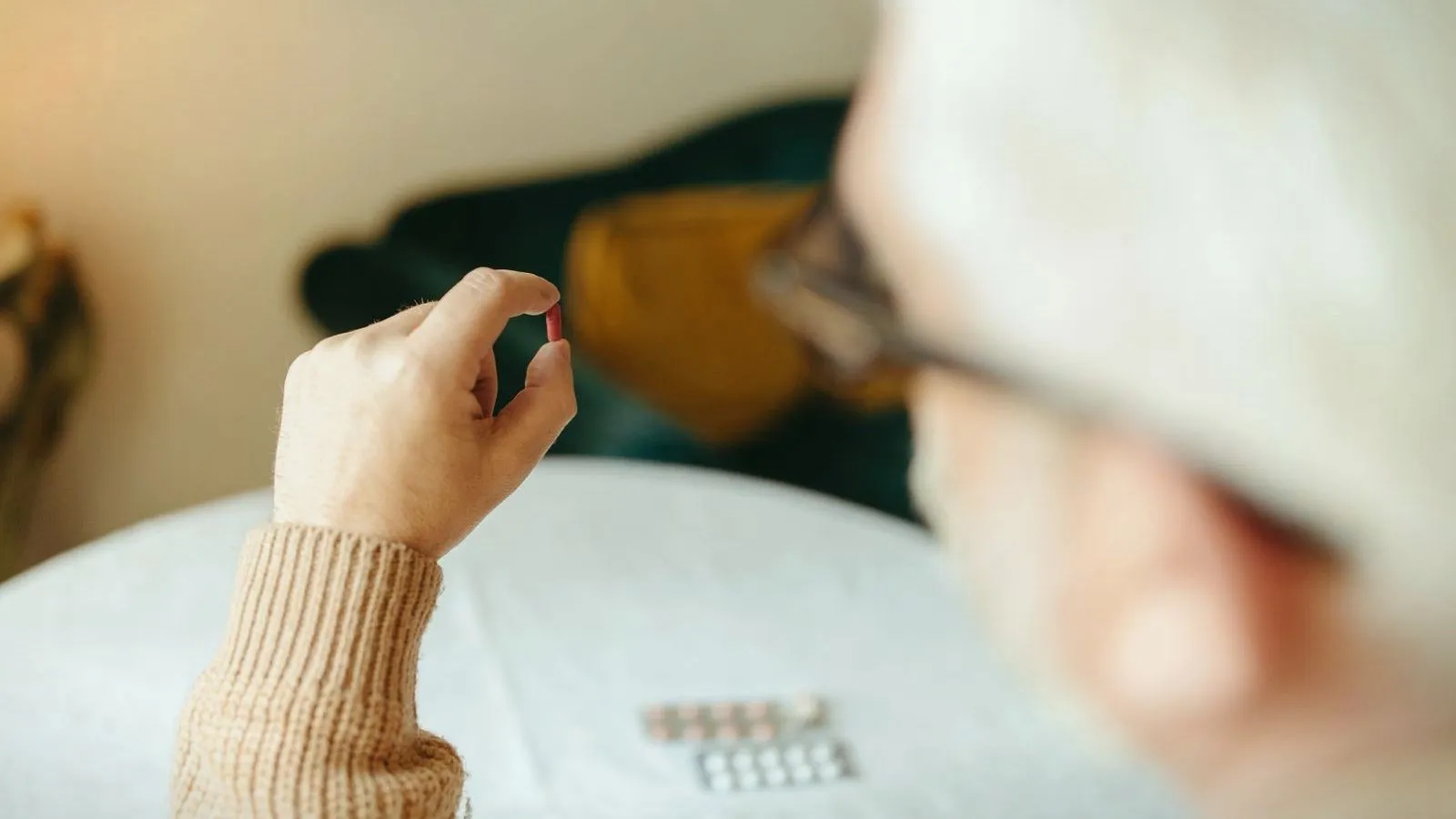 An older person holding up a single tablet, blister packs on the table in front of them