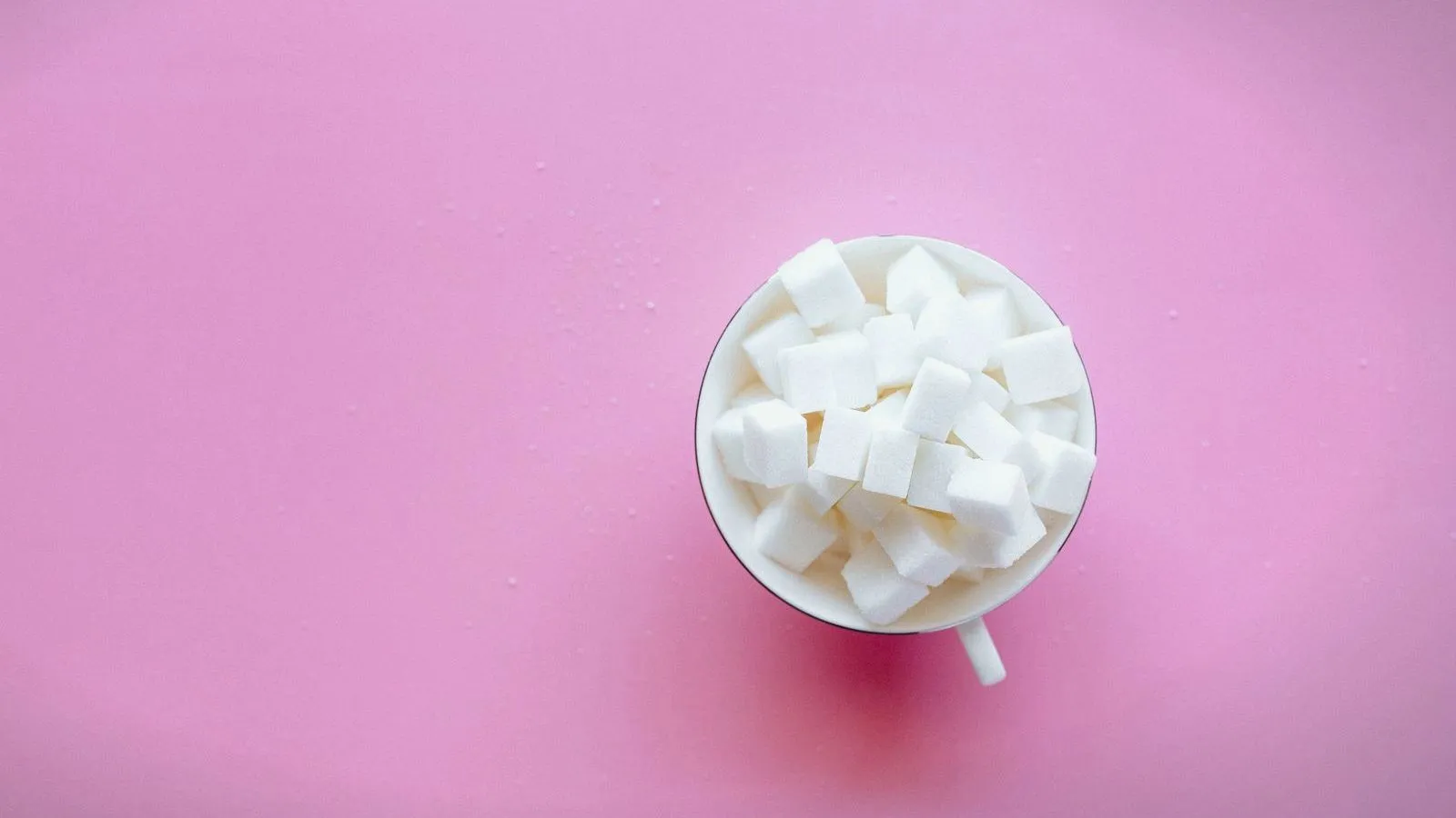 A white cup filled with sugar cubes on a pink background, seen from above