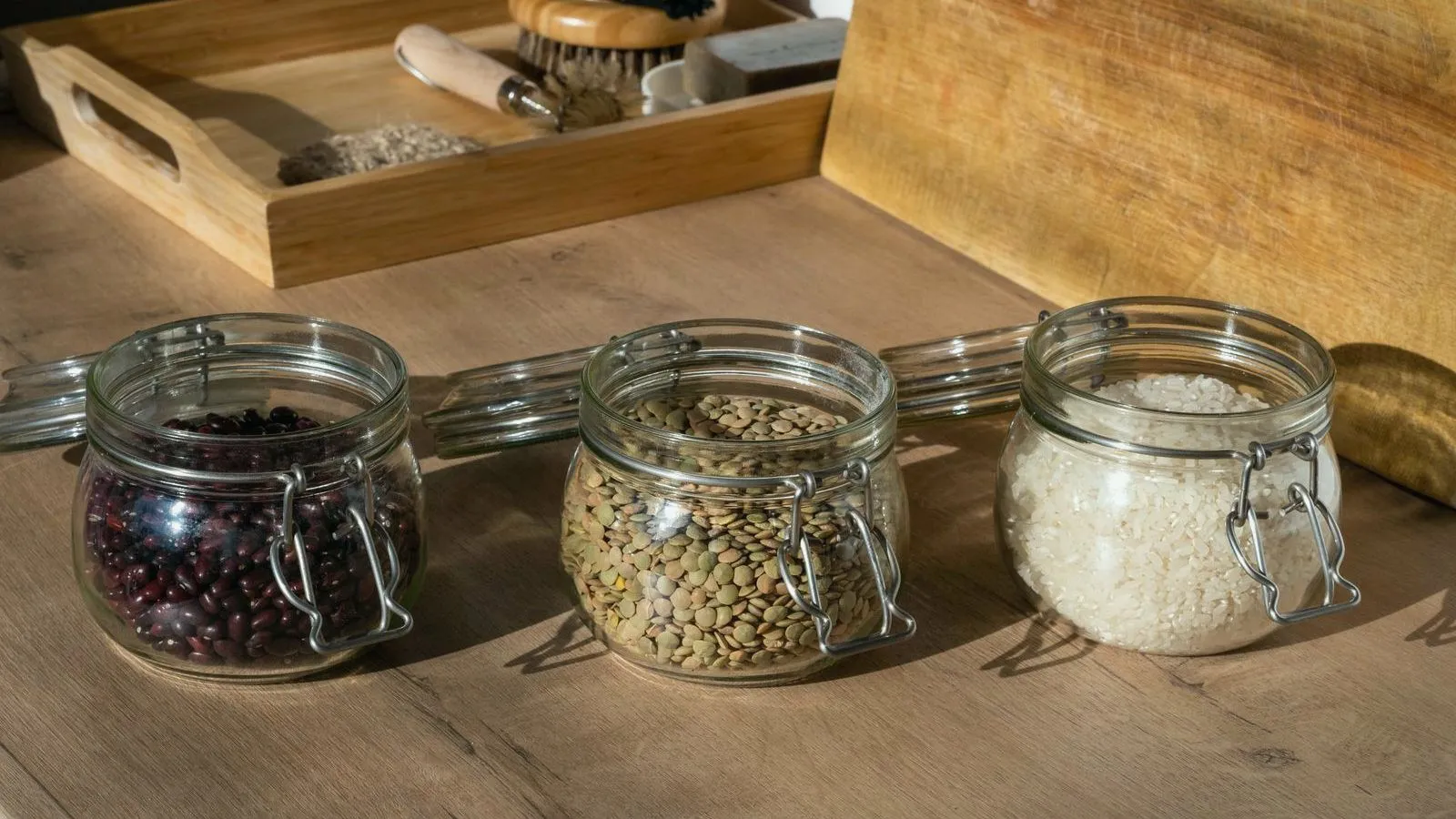 Three glass jars of dried beans, lentils and rice on a wooden counter