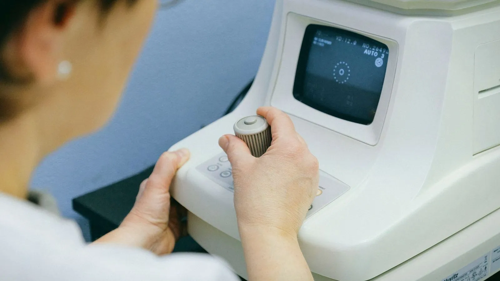 Hands operating an eye-testing instrument with a small screen.
