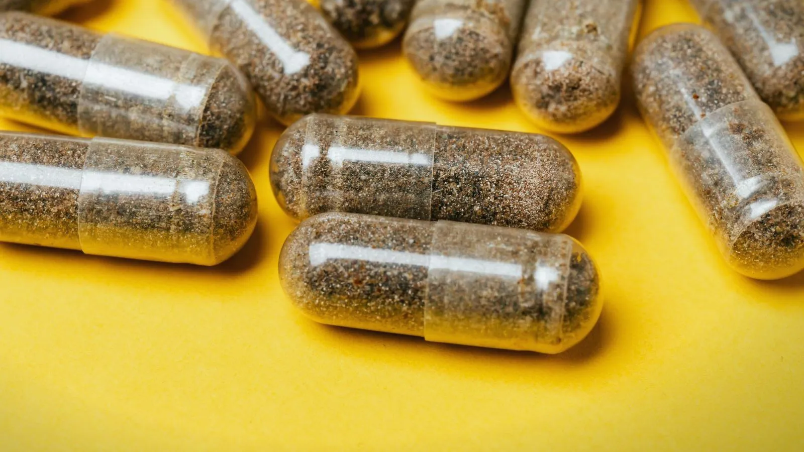 Clear capsules filled with speckled brown powder lie scattered on a bright yellow surface.