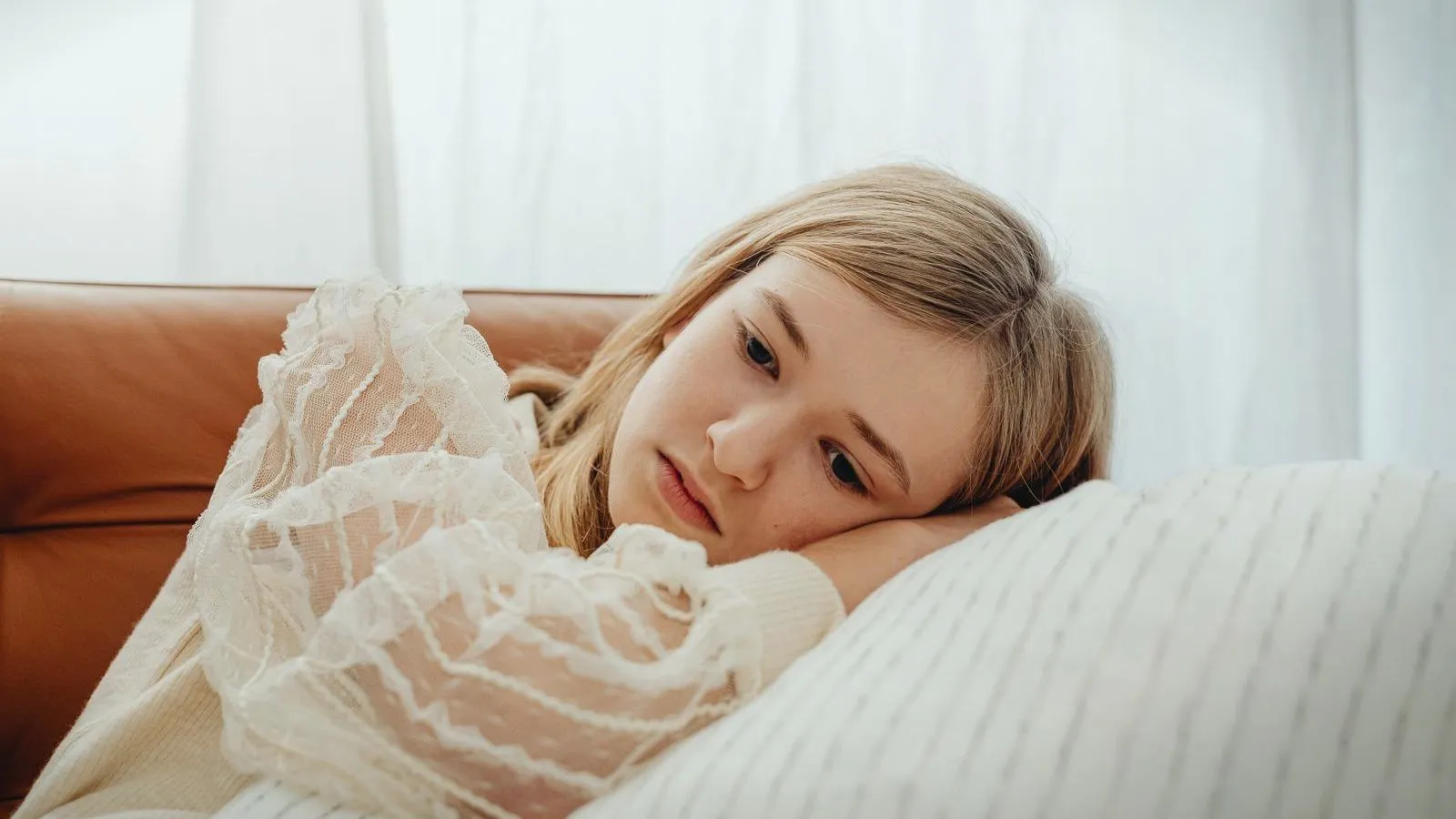 A teenage girl resting her head on her arm on a sofa, looking pensive