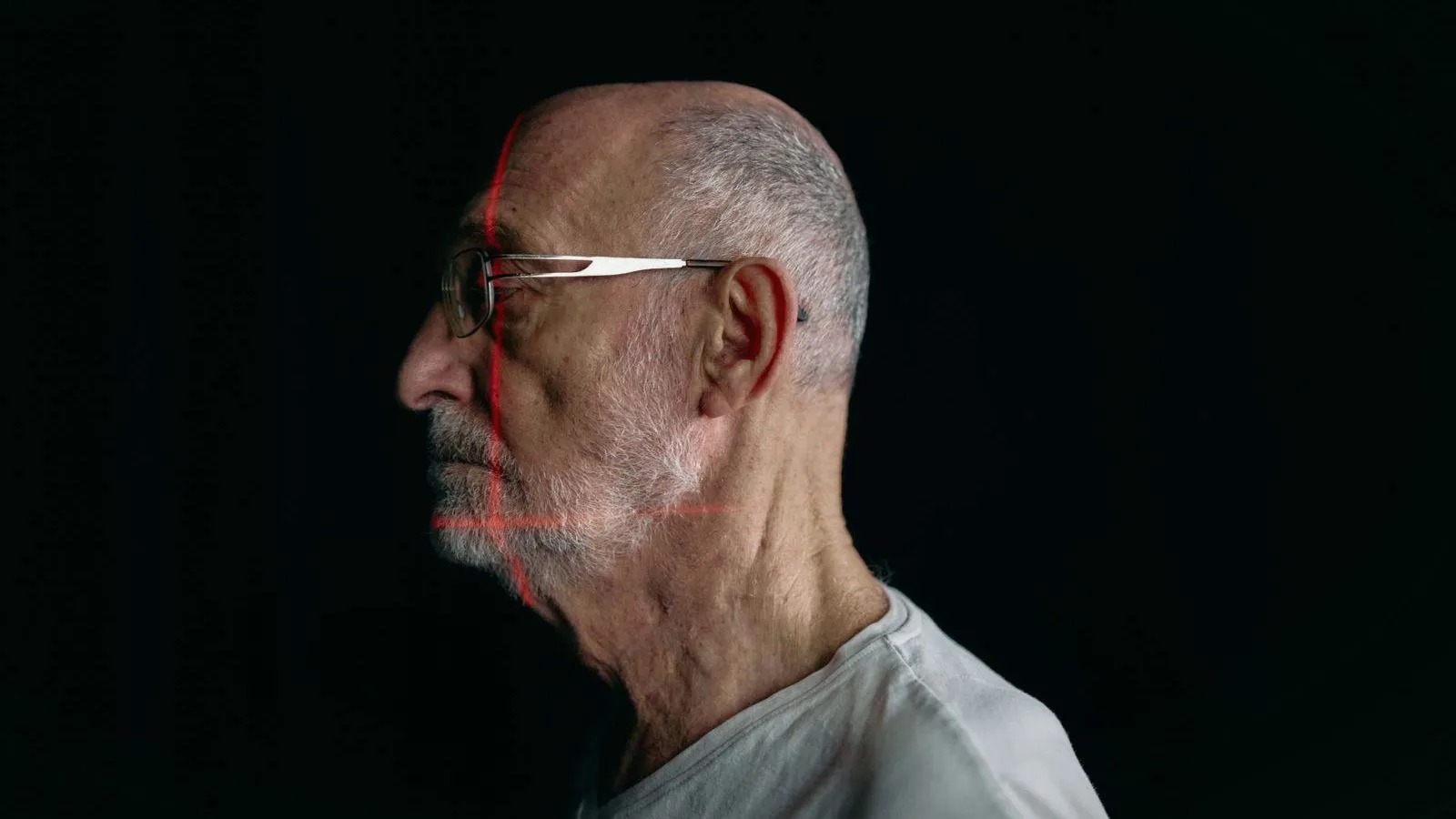 An older man in profile against a black background, a thin red line crossing his face