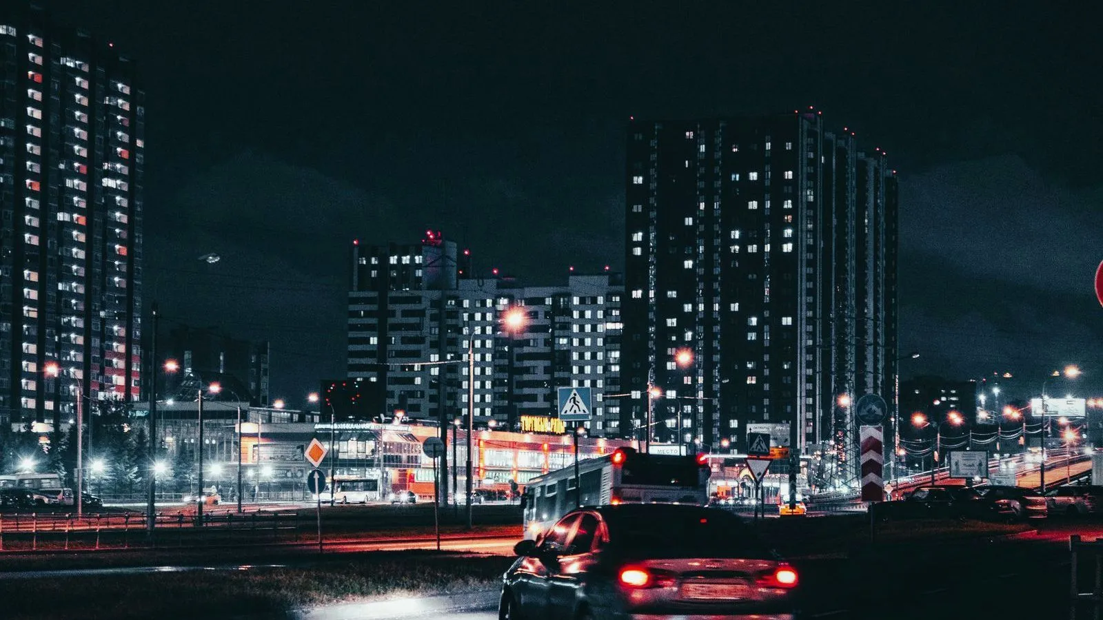 Cars on a road at night below lit apartment towers.