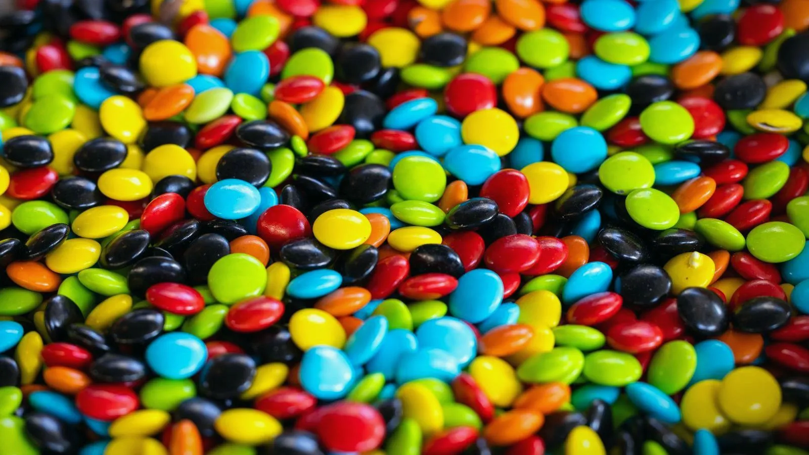 A dense field of brightly colored candy-coated sweets in red, blue, green, yellow and black