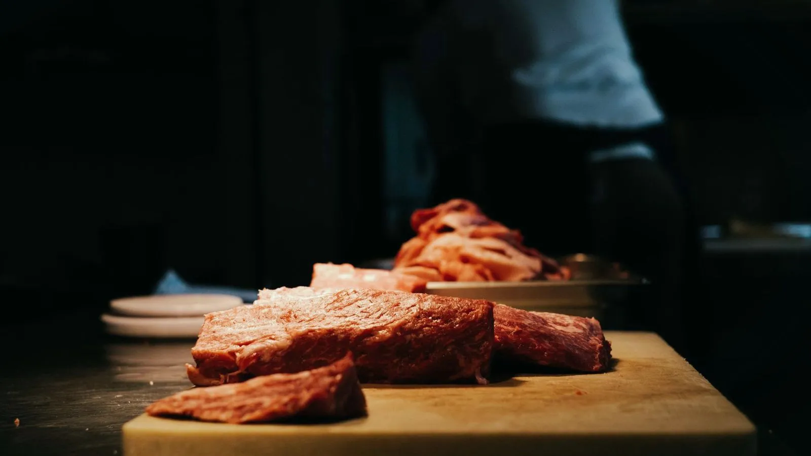 Sliced raw beef resting on a wooden board in a dark kitchen