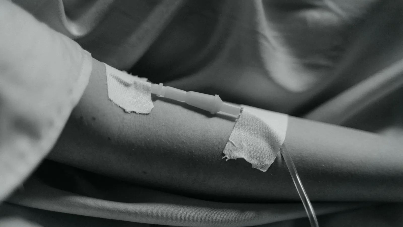 A cannula taped into a patient forearm during an infusion, in black and white