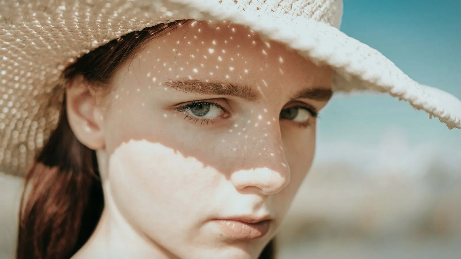 Sunlight dappled through a straw hat across a face