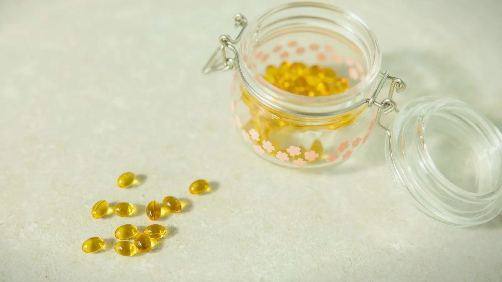 A glass jar of yellow softgel capsules with several spilled onto a pale surface