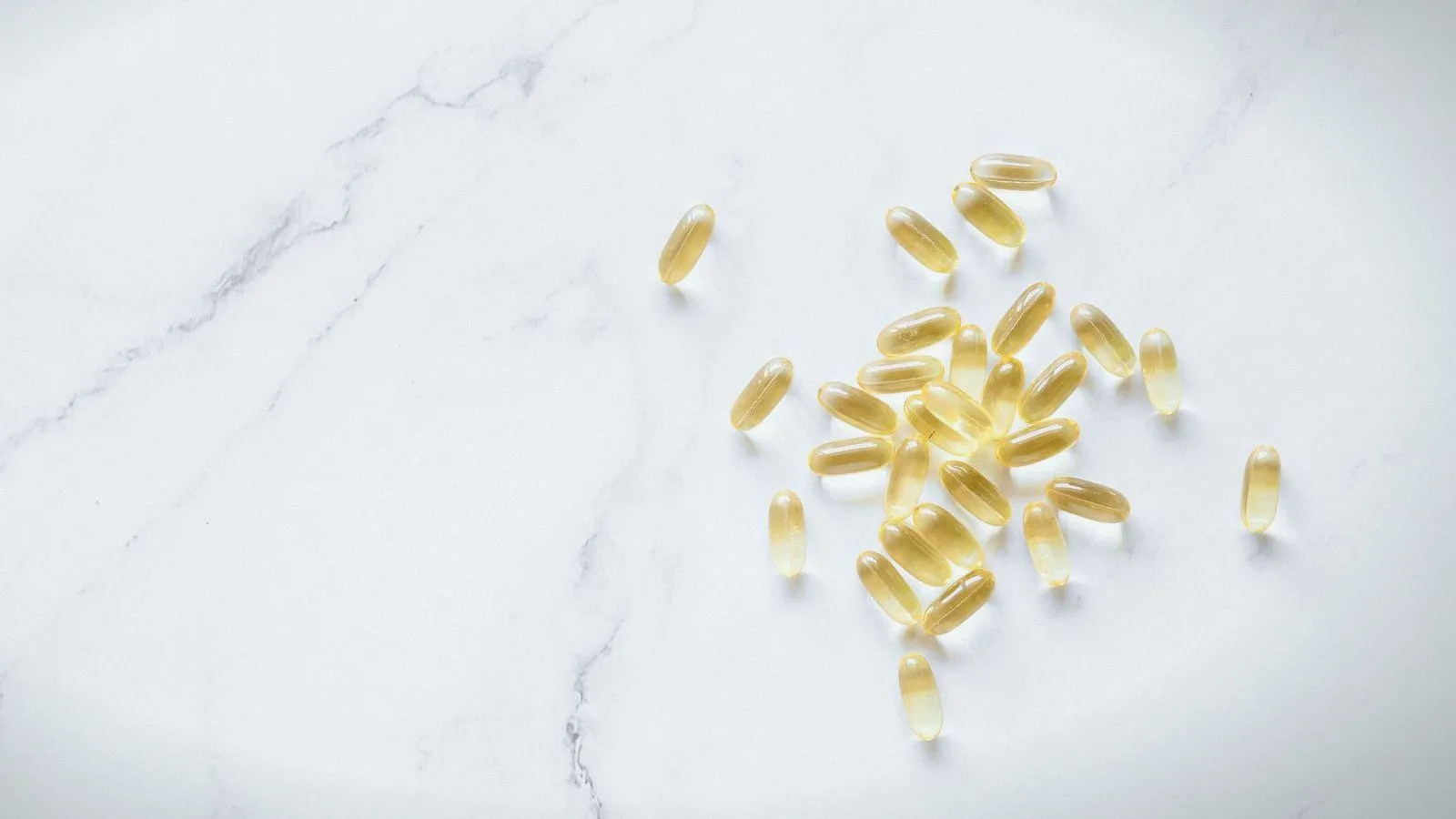 Small clear yellow softgel capsules scattered across a white marble surface