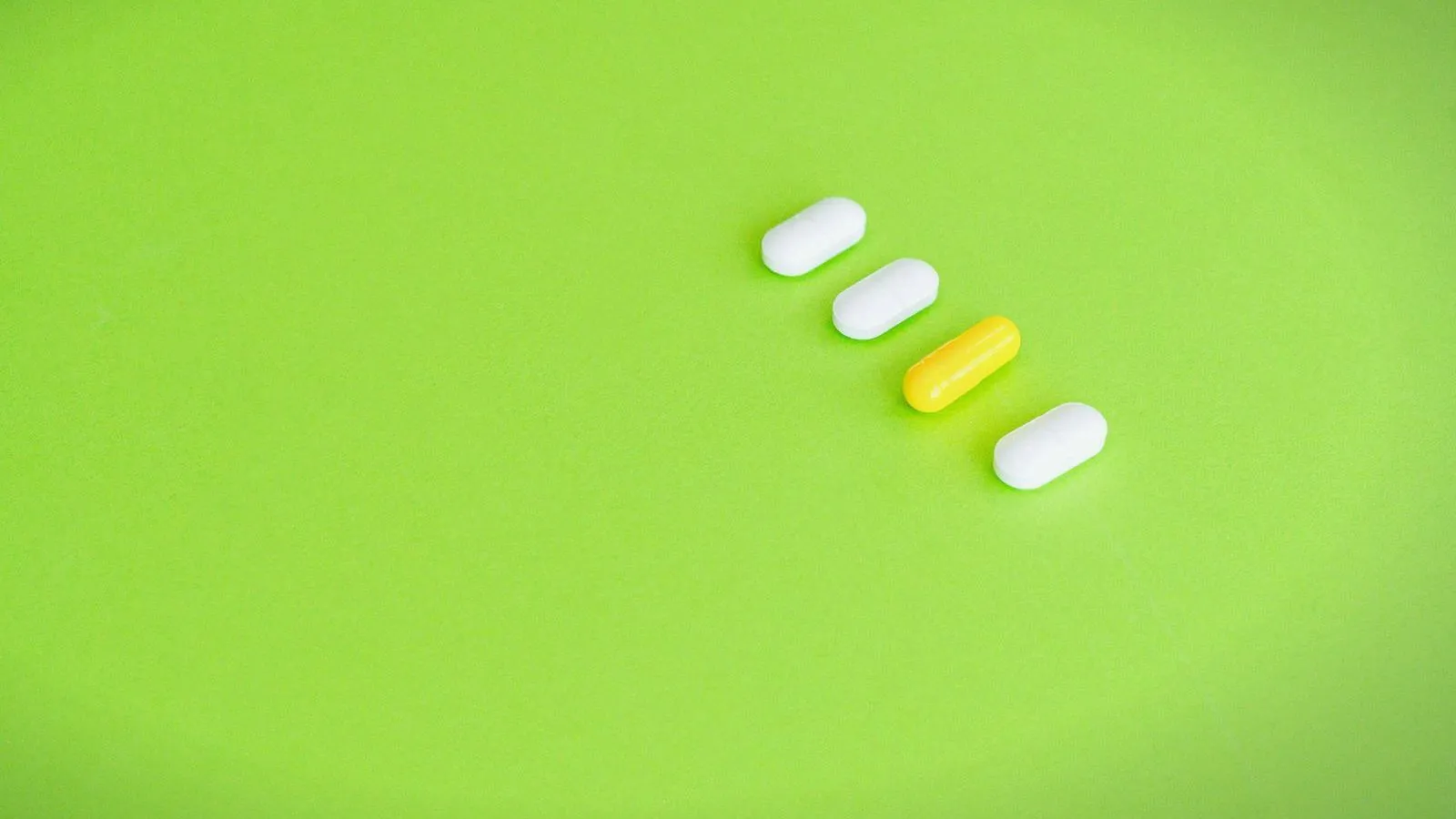 Three white tablets and a yellow capsule in a row on a green background.