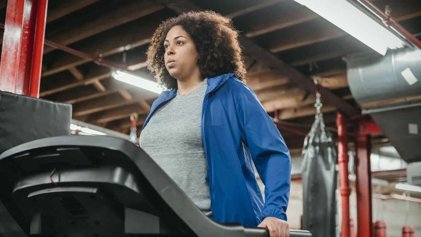A person in a blue jacket walking on a treadmill in a gym.