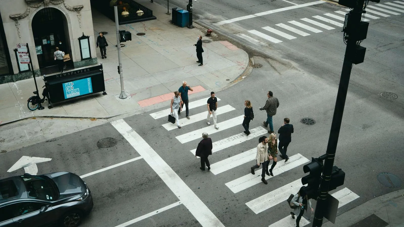 An overhead view of people crossing a city street at a marked crosswalk