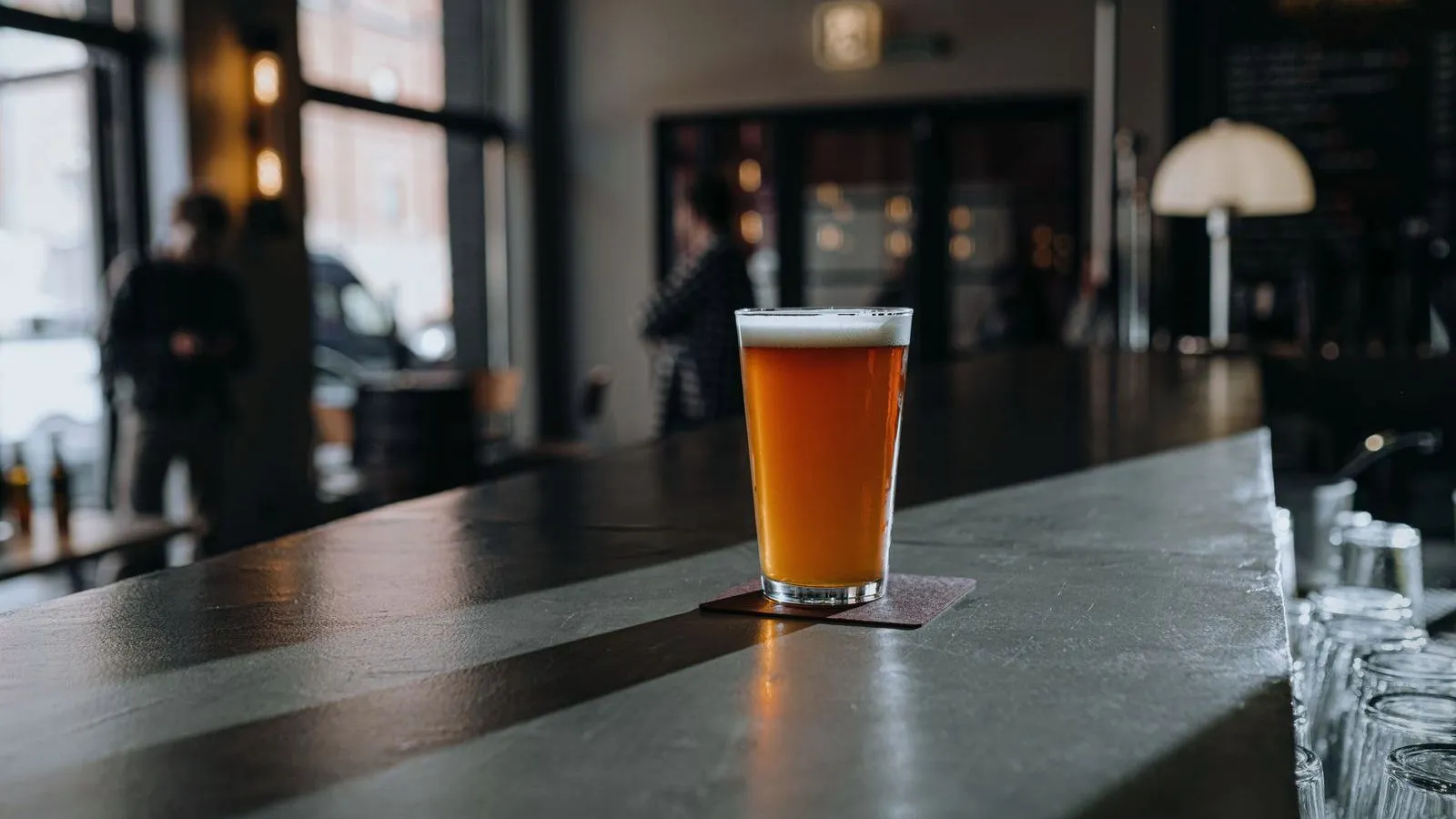 A glass of beer on a bar counter in afternoon light, empty glasses lined up beyond it