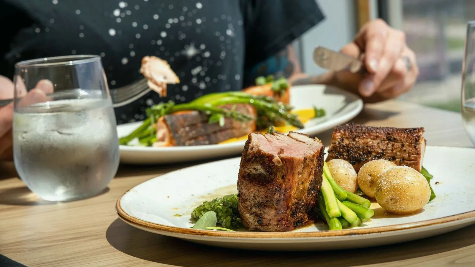 A glass of water beside a plated meal, with someone eating at the same table