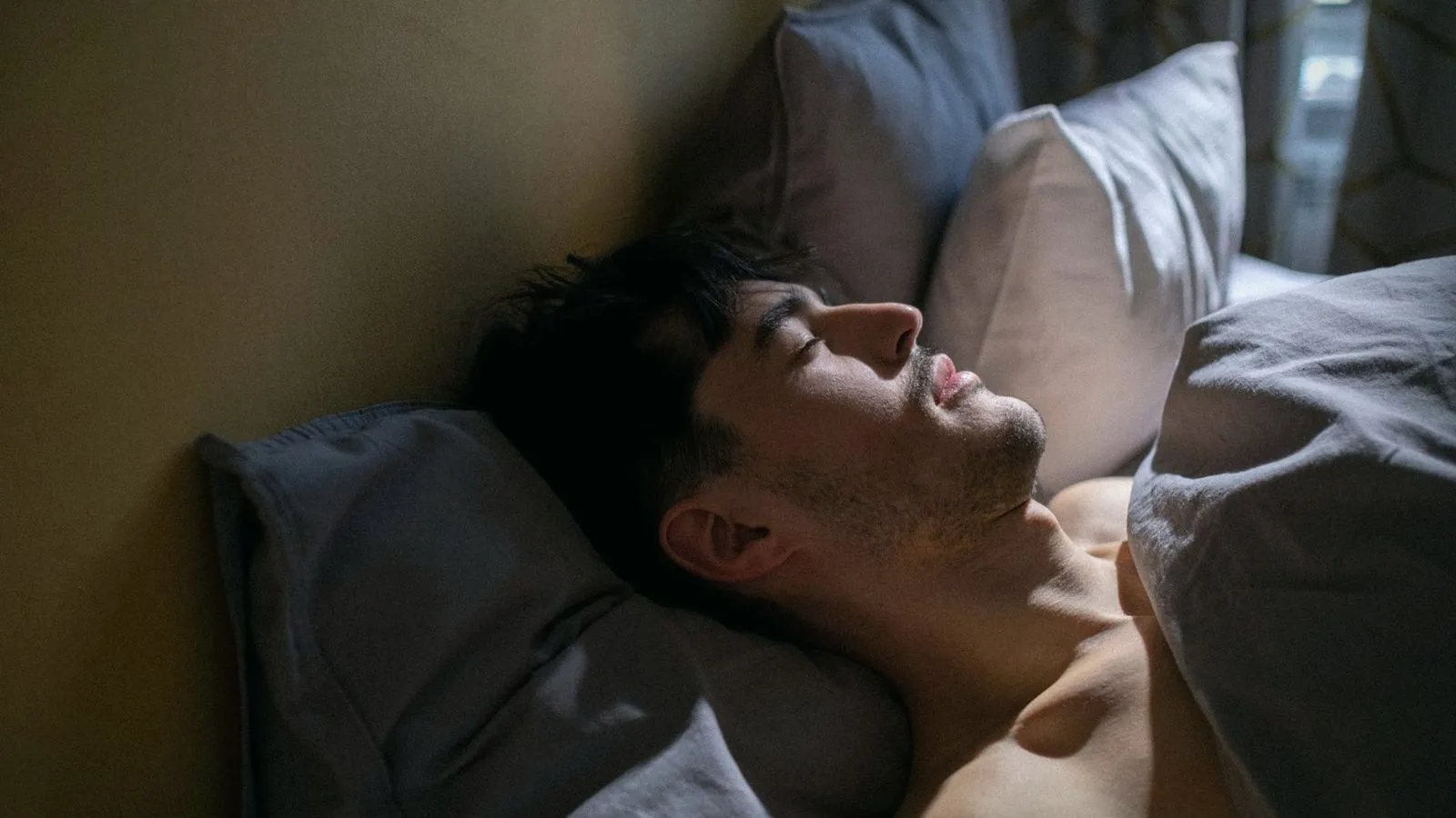 A man asleep on his back in bed in soft light