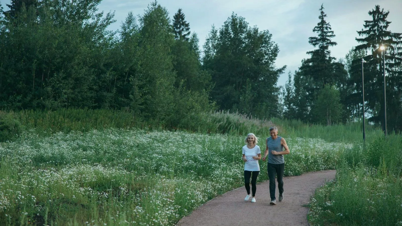 Two people running side by side along a path through a meadow of white wildflowers