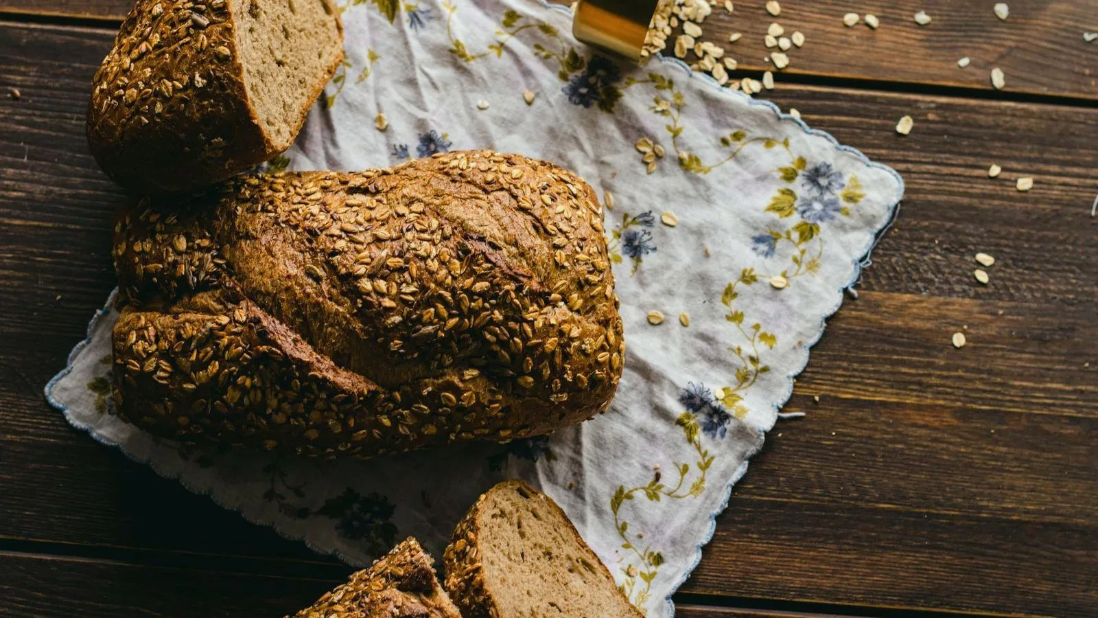 Seeded wholemeal loaves and slices on a cloth on a wooden table