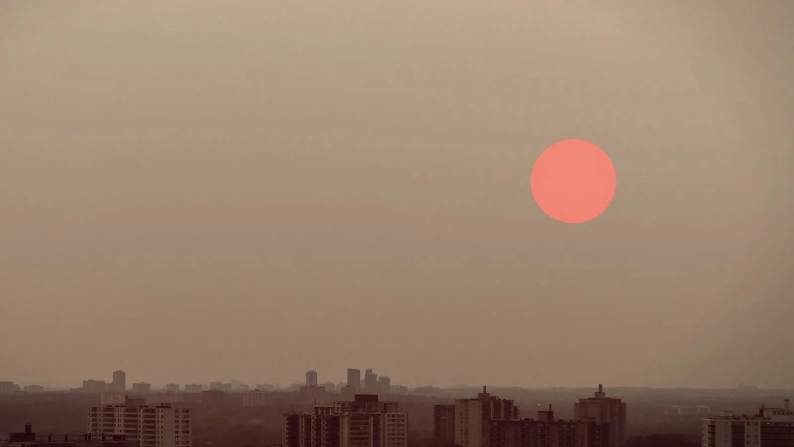 A red sun showing through thick haze above a faint city skyline