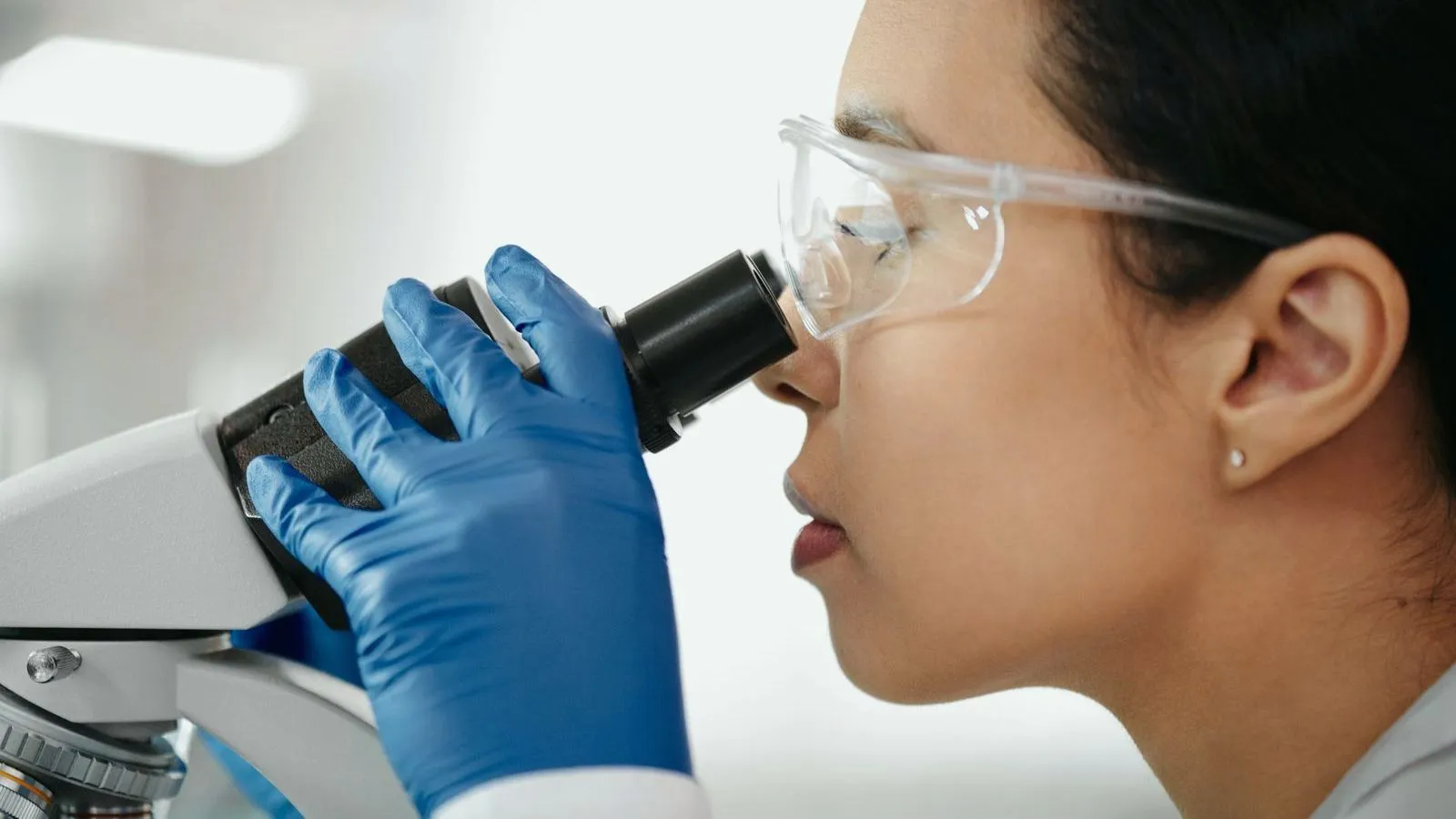 A researcher in safety goggles looking into a microscope